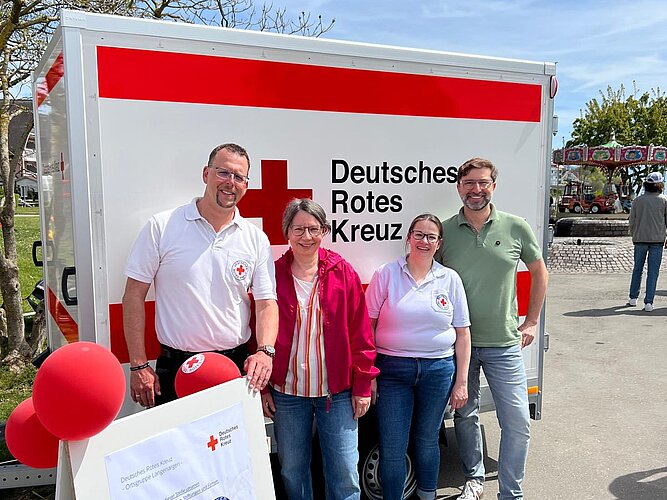 Birgit und Alex Böhm von PAKO stehen mit dem Team der DRK Ortsgruppe Langenargen vor dem neuen Einsatzhänger.