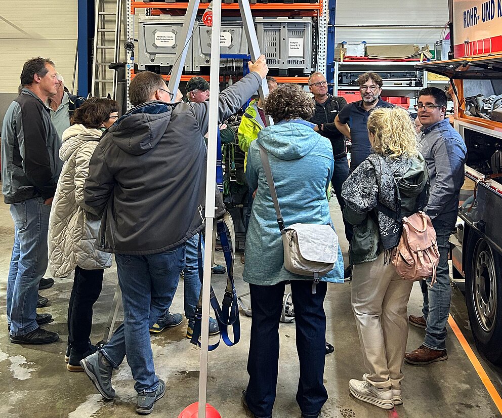 Betriebsbesichtigung Personengruppe bei einer Führung durch eine Werkhalle mit Lagerregalen, Krananlage und Einsatzfahrzeug.