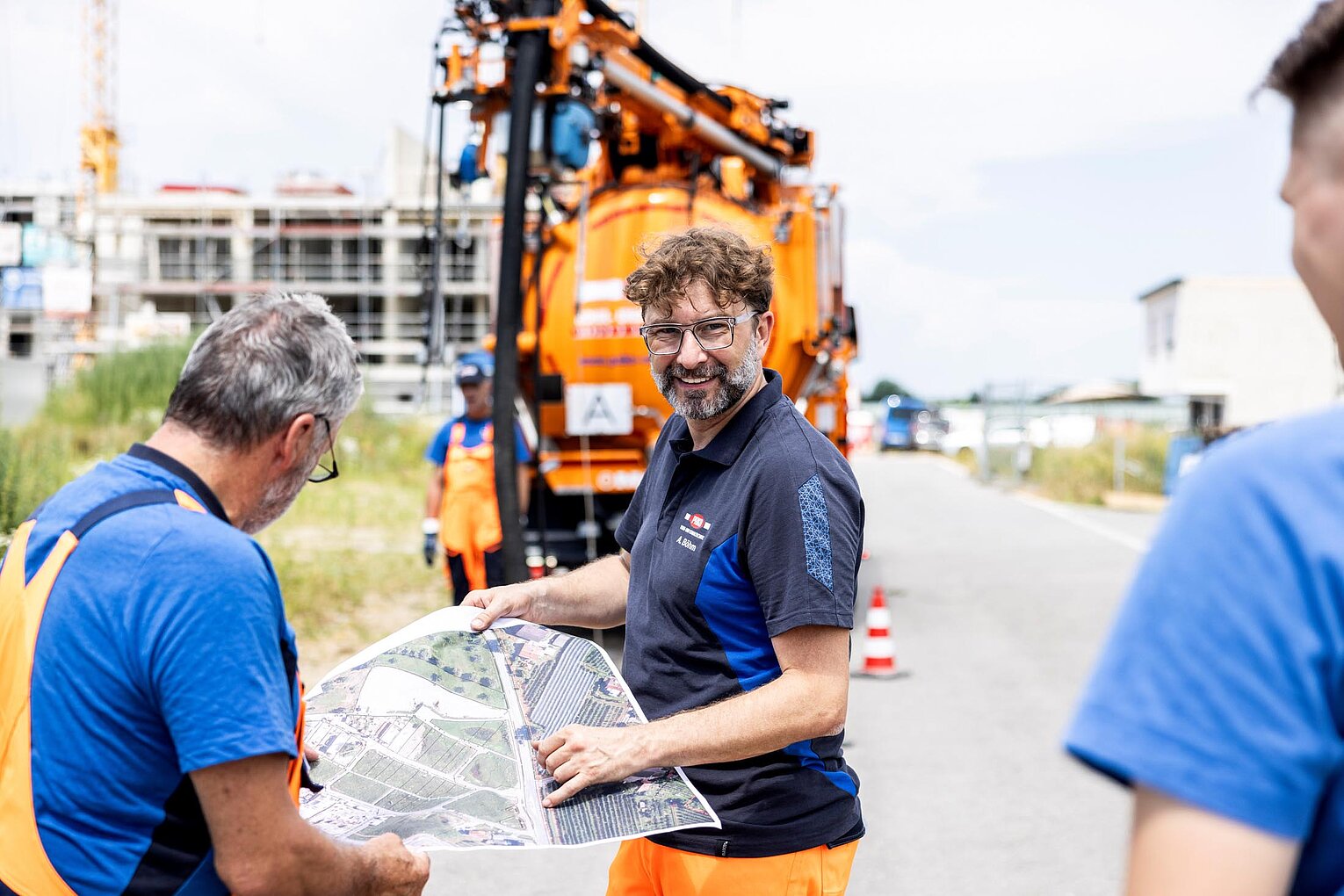 Mehrere PAKO-Mitarbeiter in blauer Arbeitskleidung arbeiten gemeinsam an einem orangefarbenen Kanalreinigungsfahrzeug auf dem Betriebshof.