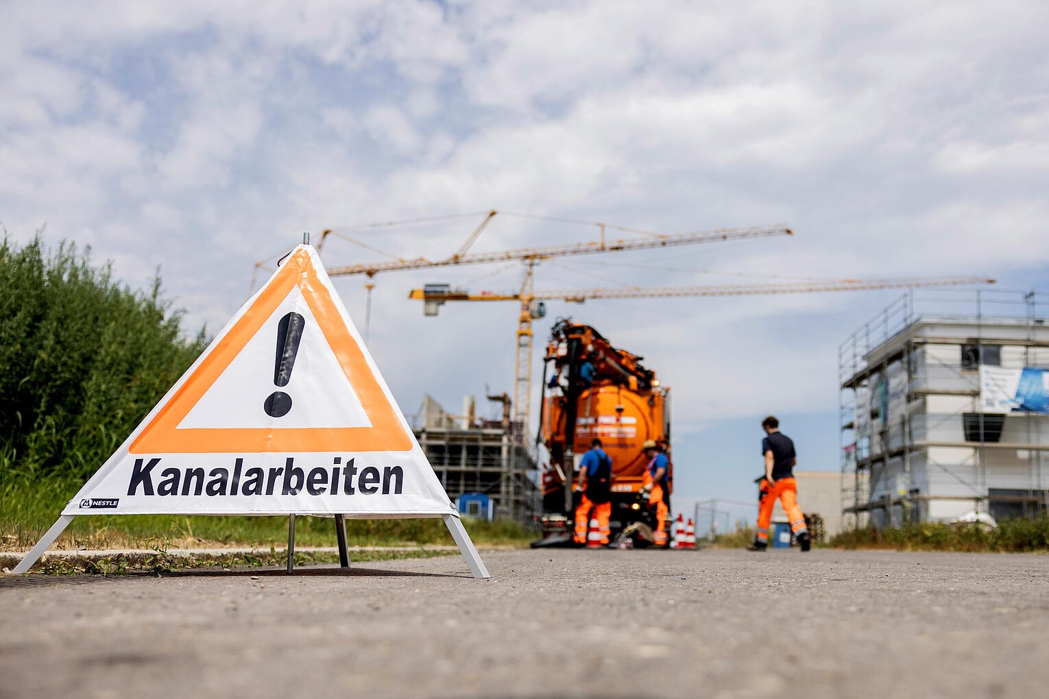 Baustelle mit PAKO-Fahrzeug PAKO-Fahrzeug auf einer Straße im Einsatz, davor ein Baustellenschild mit Warnhinweis und Absperrung.