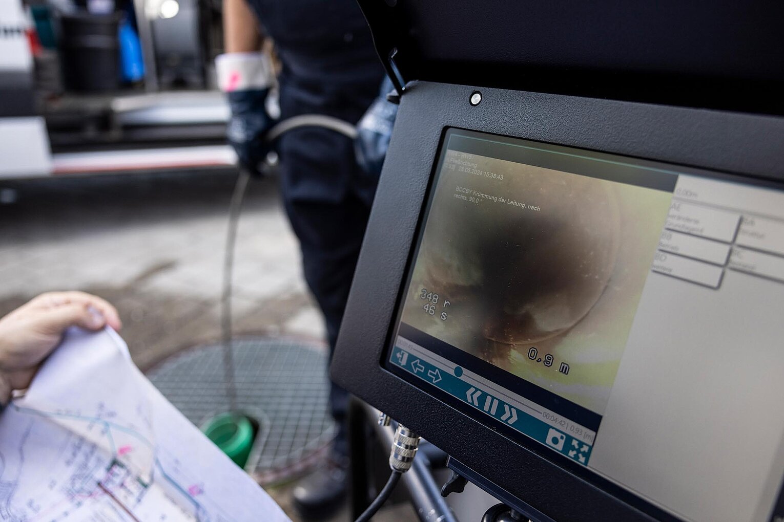 Monitor zeigt Livebild einer Kamerainspektion im Rohr, technisches Equipment im Hintergrund sichtbar.