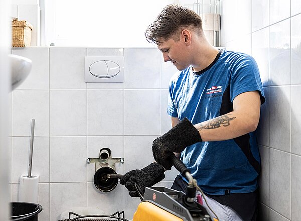 Mechanische Abflussreinigung im Bad PAKO-Fachkraft reinigt Abfluss in einem Badezimmer mithilfe einer mechanischen Rohrreinigungsspirale